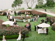 a group of people standing around tables and umbrellas in the grass with flowers on them