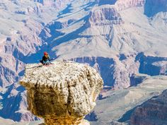 a person sitting on top of a large rock in the middle of a mountain range