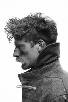 a black and white photo of a man with curly hair looking to the side while wearing a jacket