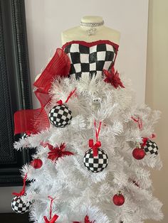 a white christmas tree with red and black ornaments on it's top, next to a mannequin