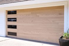 a wooden garage door with two windows and plants in the planter on the side