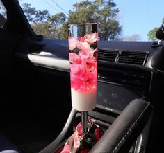 a vase with pink flowers in it sitting on the dashboard of a car