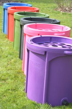 there are many different colored trash cans in the grass, one is purple and one is green