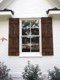 a white brick house with two brown wooden shutters on the windows and plants in front