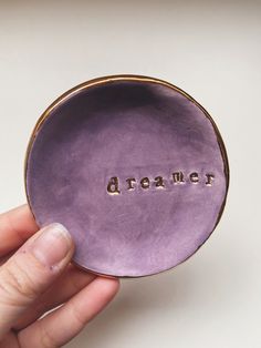 a hand holding a purple ceramic bowl with the word dream written in gold on it