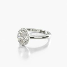 an oval shaped diamond ring with a halo setting in white gold, on a plain surface