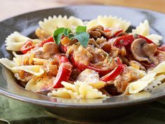 pasta with mushrooms and peppers in a black bowl on a green napkin next to a wooden table