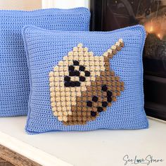 two blue crocheted pillows sitting on top of a white shelf next to a framed photo