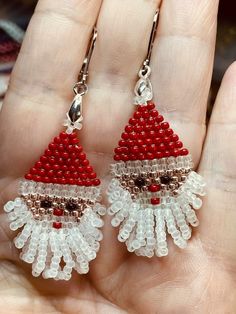 a pair of red and white beaded santa claus earrings on a person's hand