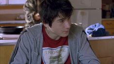 a young man sitting at a kitchen table looking off to the side in front of him