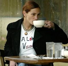 a woman sitting at a table drinking from a cup