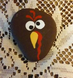 a rock with a turkey face painted on it sitting on a lace tablecloth covered surface