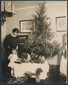 an old black and white photo of two children near a christmas tree with presents on the table