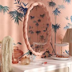 a table with a mirror, lamp and vases on it in front of a palm tree wallpaper