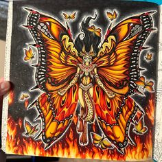 a woman holding up a drawing of a butterfly with fire and flames on it's wings