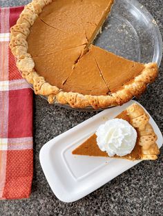 a slice of pumpkin pie on a plate next to a glass pie dish with whipped cream