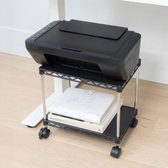 a black printer sitting on top of a cart next to a white wall and wooden floor