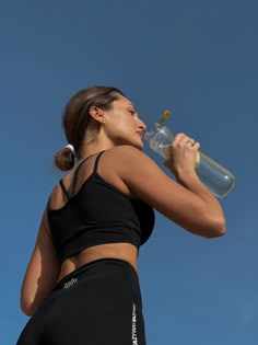 a woman drinking from a water bottle while standing in front of a blue sky with no clouds