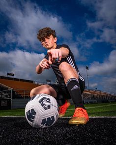 a young man sitting on the ground with a soccer ball in his hand and pointing