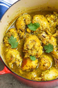 a red pot filled with chicken curry and garnished with cilantro leaves