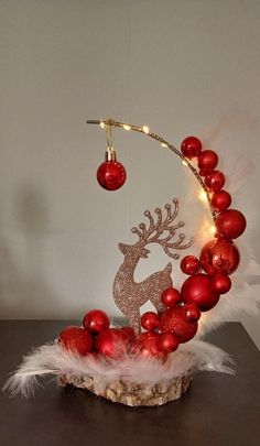 a christmas decoration with red balls and reindeer head on top of a wooden table next to a white wall