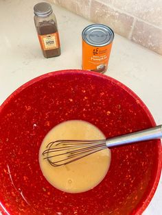 a red bowl with whisk in it next to spices and an orange can