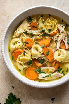 a bowl of chicken noodle soup with carrots and parsley on the side