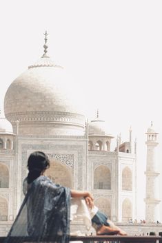 a woman sitting on a bench in front of a white building with a large dome