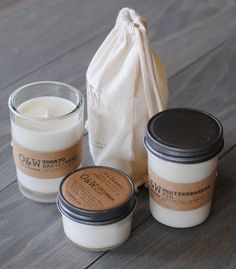 three candles sitting next to each other on top of a wooden table with a bag in the background