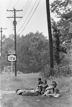 black and white photograph of four people sitting on the grass in front of a street sign