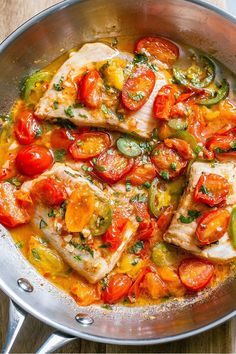 fish with tomatoes, zucchini and peppers in a pan on a wooden table