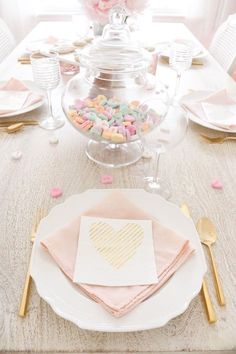 the table is set with pink and white plates, silverware, napkins, and candy