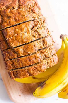 sliced banana bread sitting on top of a wooden cutting board next to two ripe bananas