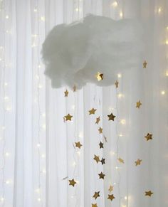 a cloud with stars hanging from it's side in front of curtained windows