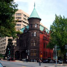 an old brick building with a green roof on the corner of a street in front of tall buildings