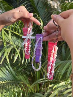 two people holding onto some colorful bracelets with pearls and bows on them, in front of plants