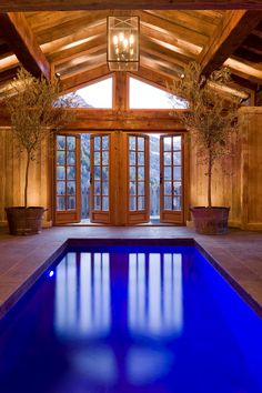 an indoor swimming pool in a large wooden building with glass doors leading to the outside