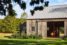 an old barn sits in the middle of a grassy field with trees and grass around it