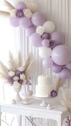 a white table topped with a cake and lots of purple balloons hanging from the ceiling