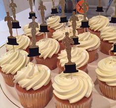 cupcakes with white frosting and gold decorations on them are arranged in rows