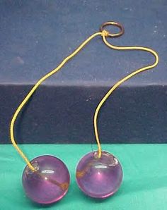 two purple glass beads are hanging from a yellow cord on a green surface with a black box behind them