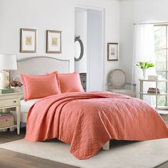 a bed with an orange comforter and matching pillows in a white room next to a window