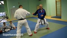 two men in white and blue uniforms are practicing karate with others sitting on the floor