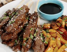 a plate with meat and vegetables on skewers next to a bowl of dipping sauce