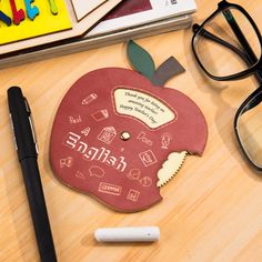 an apple shaped coaster with writing on it next to eyeglasses and other office supplies