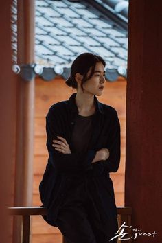 a woman sitting on top of a wooden bench next to a wall and looking off into the distance