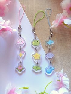 four little charms are hanging from a string on a table next to pink and white flowers