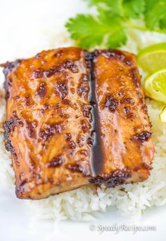 two pieces of salmon sitting on top of rice next to lemon wedges and cilantro