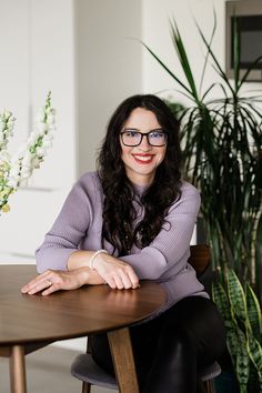 a woman sitting at a wooden table with her arms crossed and smiling for the camera