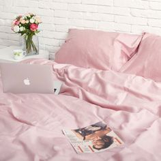 an apple laptop computer sitting on top of a pink bed in a room with white brick walls